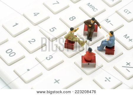 Miniature 4 people sitting on red staples placed on a white calculator. meeting or Discussion as background business concept with  copy spaces for your text or design.