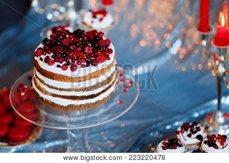 Sweet bar with muffins cakes, sweets, fruits and candle holders in area of wedding party on a silver background.