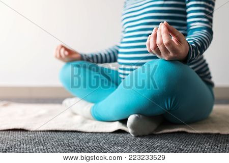 Pregnant woman practicing yoga exercise at home. Pregnancy yoga and indoors fitness concept. Ungraded low contrast footage with natural window light.