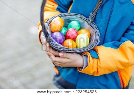 Close-up of hands of little child with colorful Easter eggs in basket. Kid making an egg hunt. child searching and finding colorful eggs in domestic garden. Old christian and catholoc tradition
