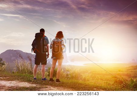 Couple of travellers with backpacks is watching at sunrise or sunset near sea bay and islands