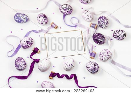 Composition with violet easter eggs, sequins and silk ribbons on a white background. Space for a greeting text. Easter, spring concept, template cards. Flat lay, top view