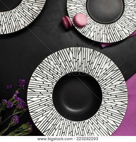 Three fancy plates on black background. Creative restaurant table setting with flowers and purple color accents
