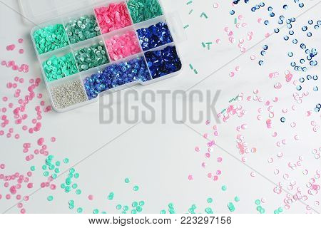 multicolored sequins on a marble background. plastic box with sparkles. creative space, flat lay, top view