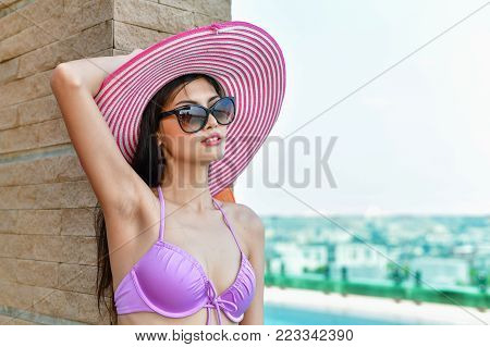 Swimsuit Concept. Beautiful girl wearing pink swimsuit. Beautiful girl in swimwear is relaxing at the swimming pool. Independent living sexy woman at the city center pool.