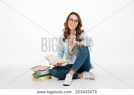 Portrait of a pretty casual girl student reading books while sitting on a floor books isolated over white background