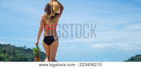 beautiful girl with a straw hat and a walking pineapple on an exotic beach, good food, rest