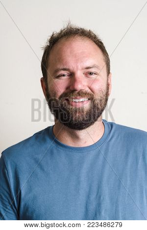 Headshot portrait of a man in a blue shirt with a dark beard on his face with simple studio lighting.