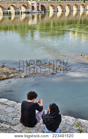 Isfahan, Iran - April 24, 2017: The Iranian couple sits on the embankment of the Zayandeh river in the spring in April, near the ancient stone bridge.