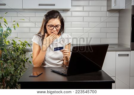 Young woman makes an online purchase with a credit card and laptop. Girl is upset because her card is locked.
