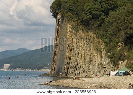 Kiseleva Mountain on background of heap of clouds with vertically standing layers of rock and sea pebbles in the foreground.