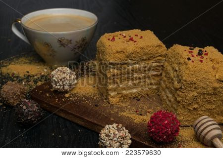 sweet homemade honey cake with truffles on a black wooden table and with coffee in porcelain cup