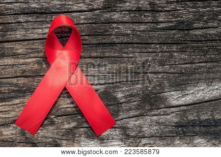 Aids red ribbon for World aids day and national HIV/AIDS and aging awareness month concept. Symbolic satin bow isolated on aged wood with clipping path