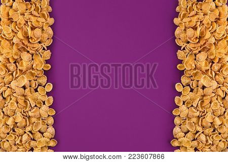 A frame lined with corn flakes. Cornflakes scattered on a purple background. Top view. Still life. Copy space. Flat lay