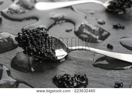 Spoon with black caviar on grey background