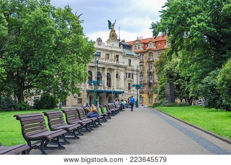 PRAGUE, CZECH REPUBLIC - JULY 21, 2009 Green park alley with benches with the view of Vinohrady Theatre (Dramatic Theater), people rest on benches