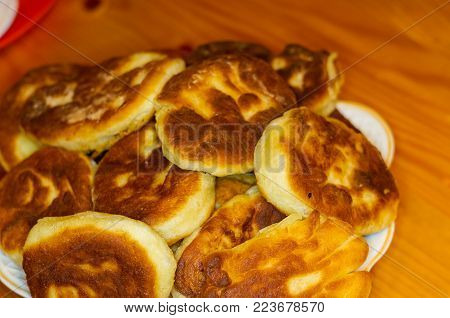 Russian pirozhki, fresh fried pasties stuffed with potatoes in a plate on a wooden table
