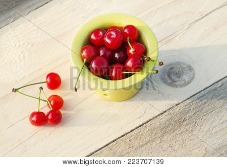 Fresh ripe cherries in a small ceramics cup on wooden table outdoors.