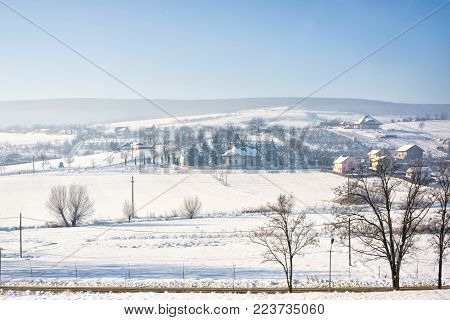 Winter landscape of romania village with snow, near Iasi city, church and houses, blue sky