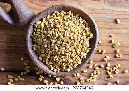 Fenugreek seeds on a wooden spoon, top view.