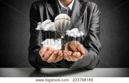 Closeup of business woman in suit presenting flying aerostate among clouds in her palms with dark wall on background. 3D rendering.