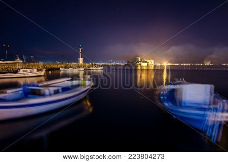 Illuminated old town of Nafplion in Greece with tiled roofs, small port, bourtzi castle, Palamidi fortress at night.