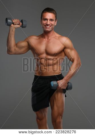 Muscular middle age man holds pair of dambells. Isolated on grey background.