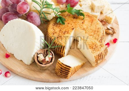Cheese platter with assorted cheeses, grapes, nuts over white wooden background, copy space. Italian cheese and fruit platter.