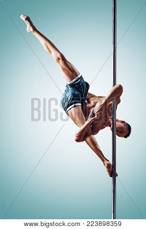 Young strong man pole dancing on blue and white background