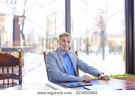 Interior designer using smart watch at cafe with tablet and roll project on table. Young handsome man waiting for business meeting. Concept of enhancing interiors of space or building to achieve healthier and more aesthetically pleasing environment for us