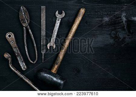 Old, rusty tools lying on a black wooden table. Hammer, chisel, metal scissors, wrench. Top view. Copy space. Still life. Flat lay