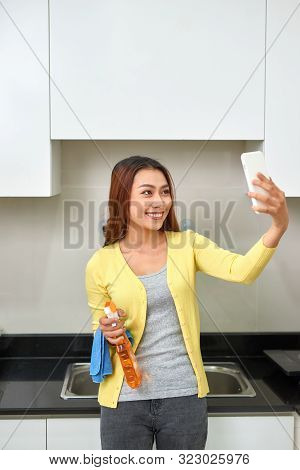 Beautiful Asian Woman Is Doing Selfie Using A Smartphone And Smiling While Cleaning Kitchen