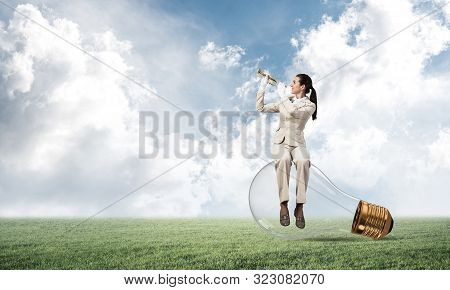 Woman Sitting On Big Light Bulb And Playing Trumpet Brass. Young Lady In White Business Suit And Glo