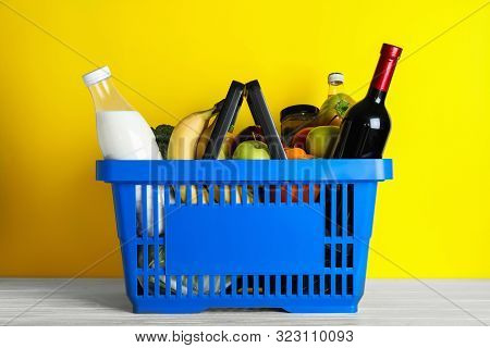 Shopping Basket With Grocery Products On White Wooden Table Against Yellow Background