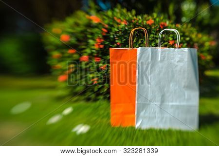 Gray And Orange Paper Bag On A Background Of Green Grass, Sky And Plants. Shoot With Lensbaby