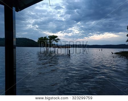 Submerged benches and tree in an artificial lake that has flooded the coast during cloudy golden hour