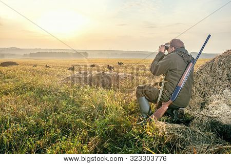 The Man Is On The Hunt. Hunting Period, Autumn Season. Male With A Gun And Binoculars At Dawn. Hant 