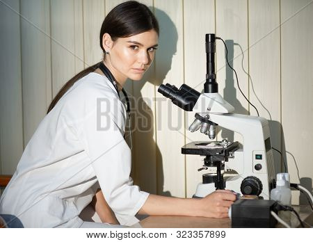 Female Doctor In White Medical Uniform With Stethoscope On Neck Looking At Specimens Under Microscop