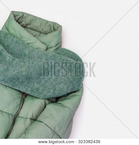 Women's Warm Clothing, Down Jacket Green Colored, Cozy Knitted Scarf On White Concrete Background. F