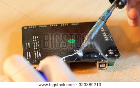 Close-up Of A Soldering Iron Melting Tin Over An Electronic Board With Visible Smoke.