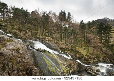 Beautiful Landscape Image Of Ogwen Valley River And Waterfalls During Winter With Snowcapped Mountai