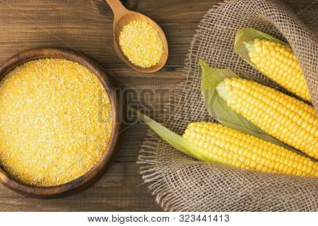 Corn Grits In A Wooden Bowl On The Background Of Fresh Corn On The Cob On A Burlap. The Concept Of T
