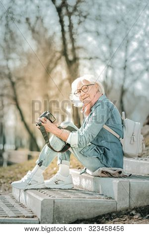 Aging Bewitching Woman Holding A Camera On The Park Steps