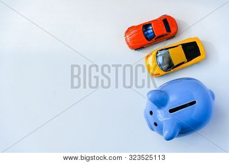 Close Up Of Blue Piggy Bank And Two Toy Cars On White Background With Copy Space. Overhead Shot.