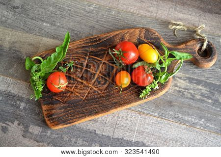 Grape Red And Yellow Tomatoes And A Laefe Of Basil On A Wooden Rustic Board Top View