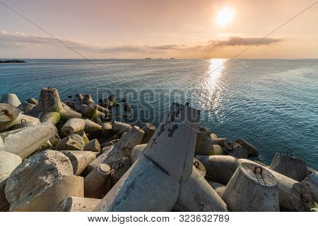 Beautiful Sunset Seascape. Breakwaters Tetrapods Ashore Of Pier. Cargo Ships On The Horizon. Travel 