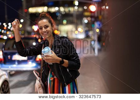 Woman calling taxi on city street at night
