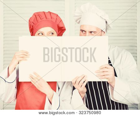 Man And Woman Chef Hide Faces Behind Open Book. Guy And Girl Read Book Recipes. Culinary Concept. Fa
