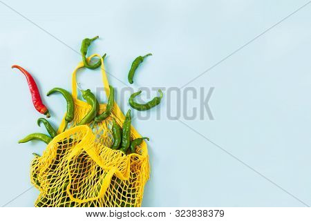 Creative Layout Green Chilli Peppers In Yellow String Bag On Pastel Blue Background. Heap Of Green H
