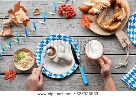 Oktoberfest Traditional Food And Beer. Hands Holding Beer Mug And Fork With White Sausage, Pretzels 